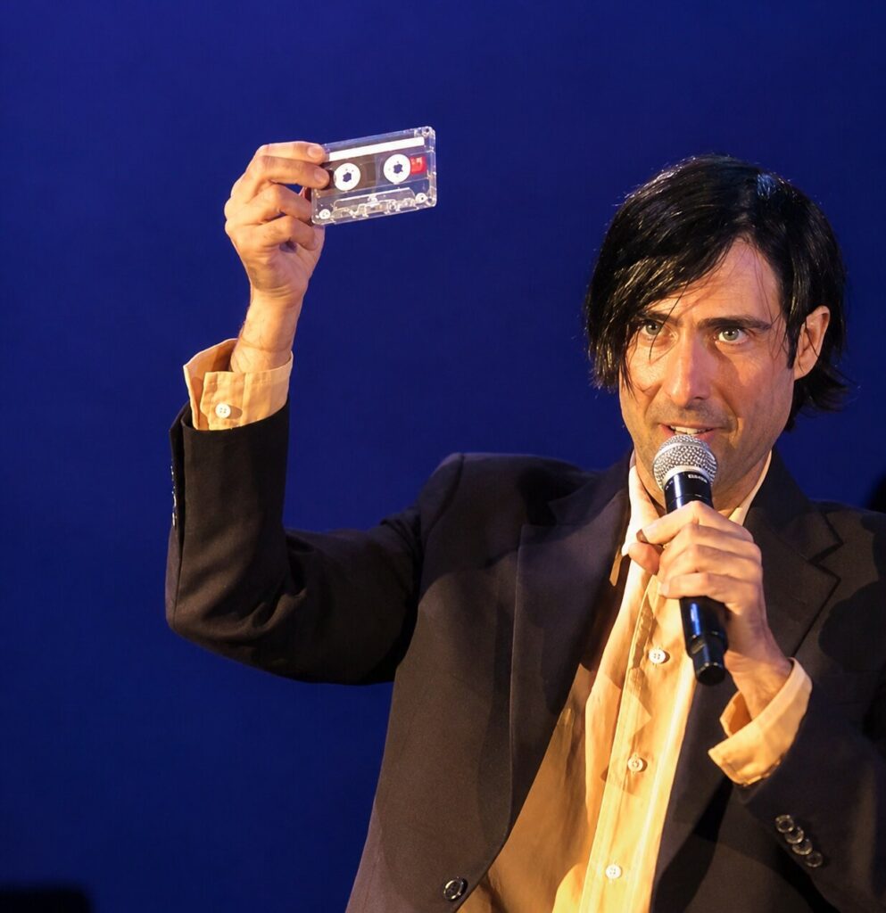 Jason Schwartzman holds up his Rushmore cassette tape on stage